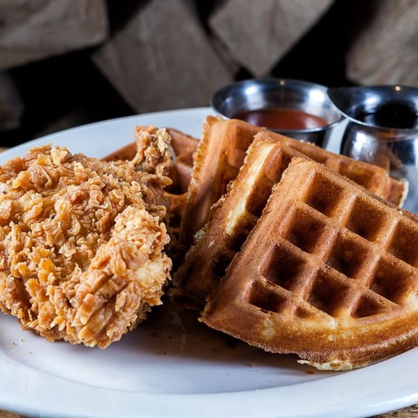 Crispy fried chicken and waffles with syrup and hot sauce on a white plate.