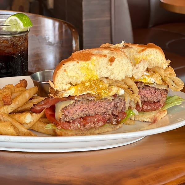 A juicy burger with bacon, fried egg, and crispy onions, served with fries and a drink.