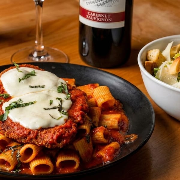 Chicken parmesan with rigatoni pasta, Caesar salad, and a bottle of Cabernet Sauvignon.