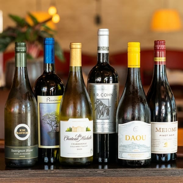 Six bottles of various wines, including Sauvignon Blanc, Chardonnay, and Pinot Noir, on a bar.