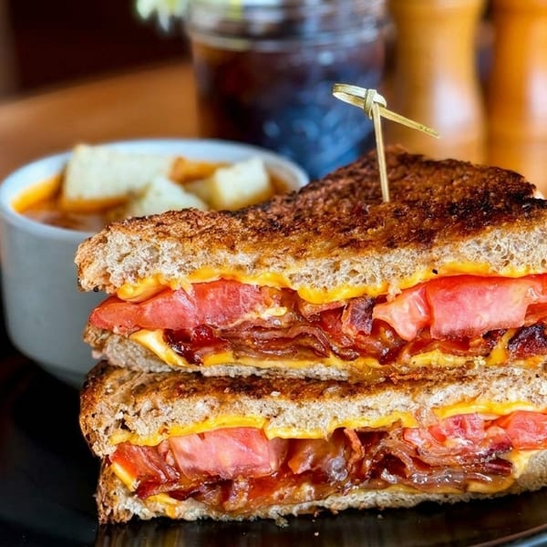 Grilled cheese sandwich with bacon and tomato, served with a side of tomato soup.