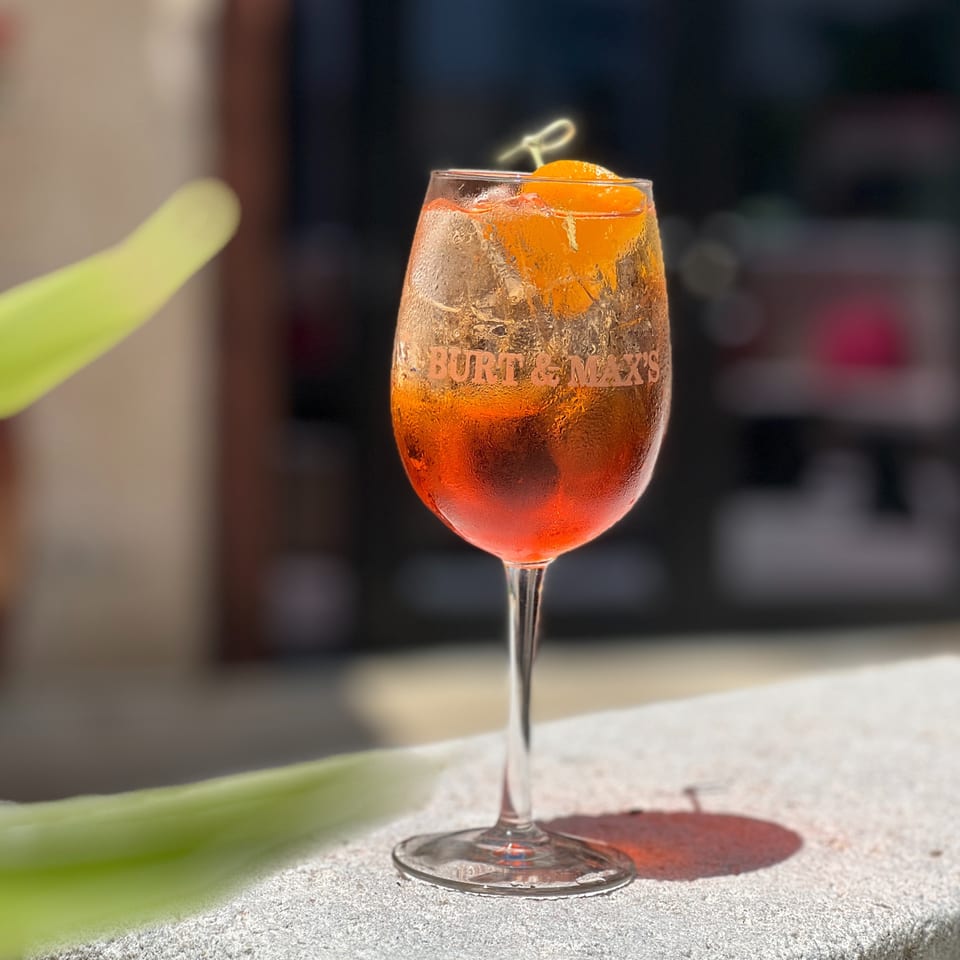 Orange cocktail in a stemmed glass garnished with citrus peel, displayed on a sunlit stone table.