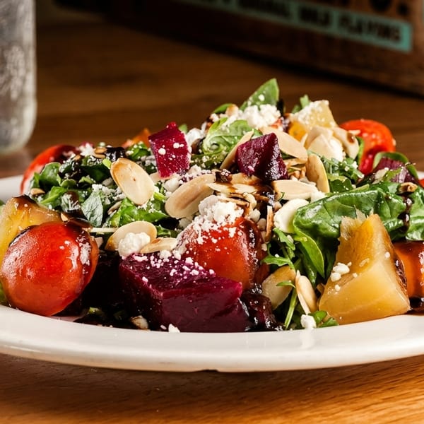 Colorful salad with beets, tomatoes, pears, greens, feta, almonds, and balsamic glaze.