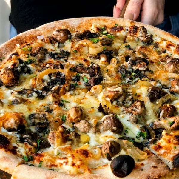 A person holding a large, freshly baked mushroom and onion pizza with a crispy crust.