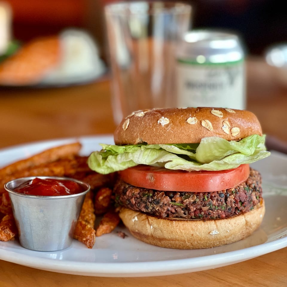 Plant-based burger with lettuce, tomato, and oat-topped bun served with fries and ketchup on a plate.