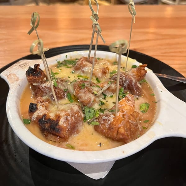 A white dish filled with cheesy, saucy shrimp, garnished with parsley and small bamboo skewers.