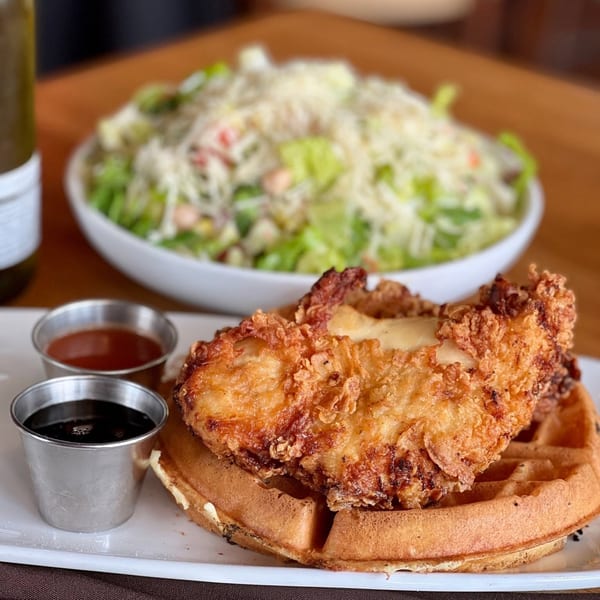 Crispy fried chicken and waffles with syrup, hot sauce, and a side salad.
