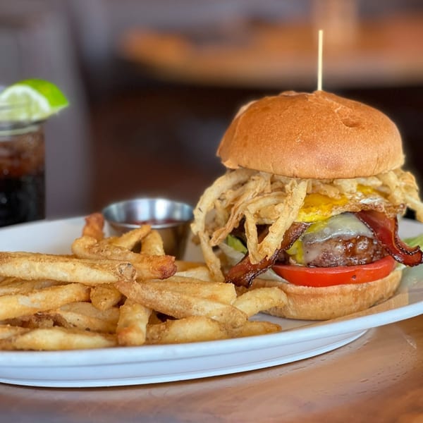 A gourmet burger with bacon, fried egg, crispy onions, and fries on a white plate.
